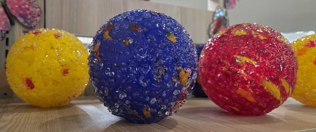 An image of 4 spheres--yellow, red, and deep blue with grooved surface specifically designed to serve as a drinking ball for bees and butterflies.